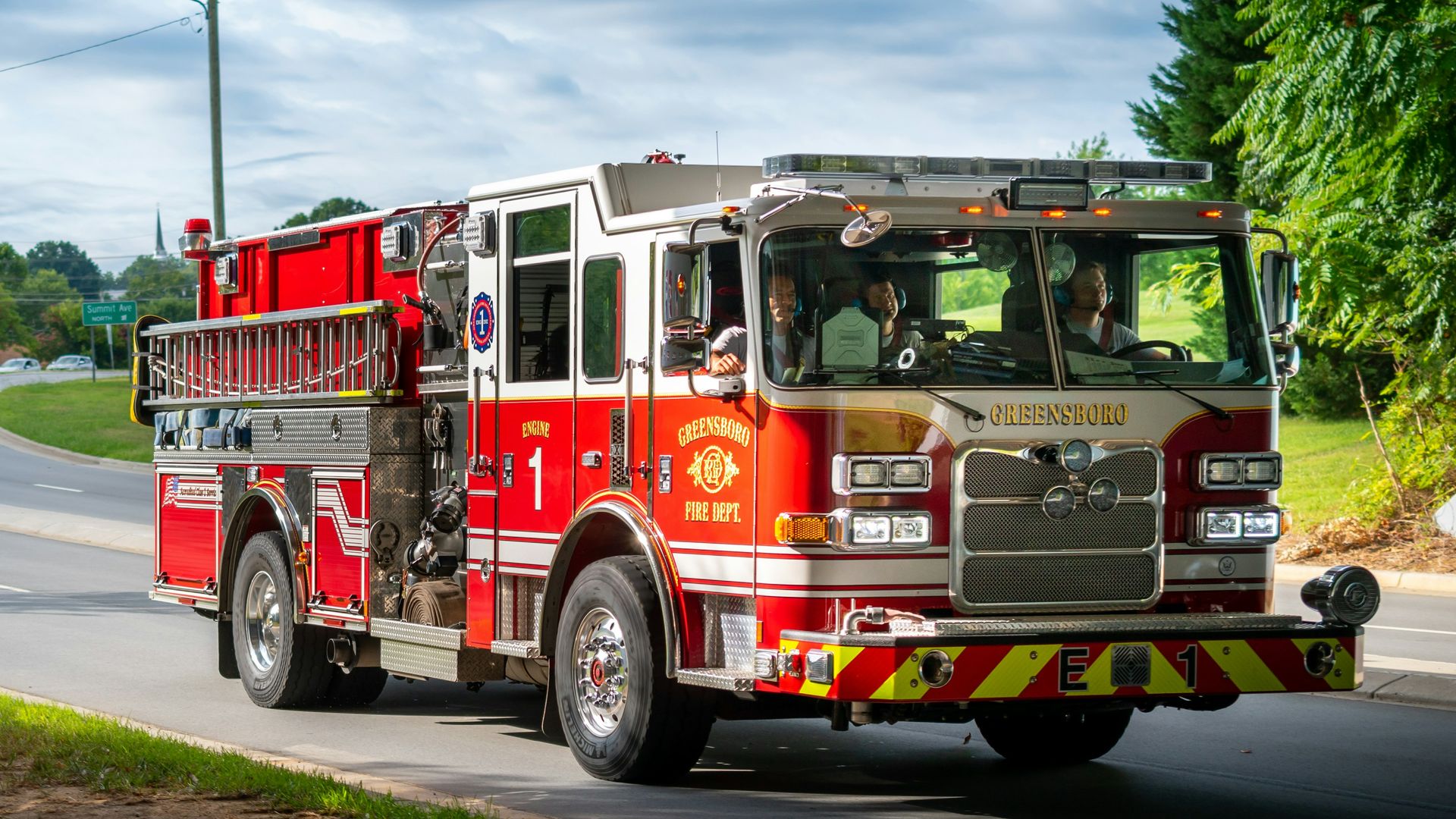 Red fire engine driving along a tree-lined road on a summer day